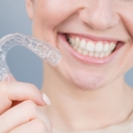 Close-up portrait of a woman holding a clear orthodontic aligner near her smile