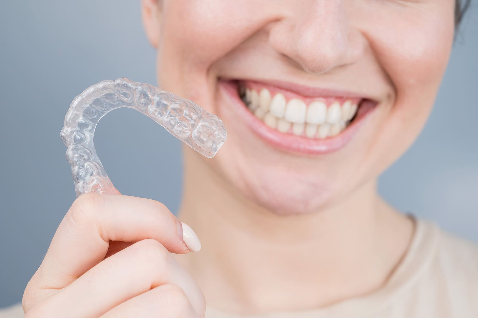 Close-up portrait of a woman holding a clear orthodontic aligner near her smile