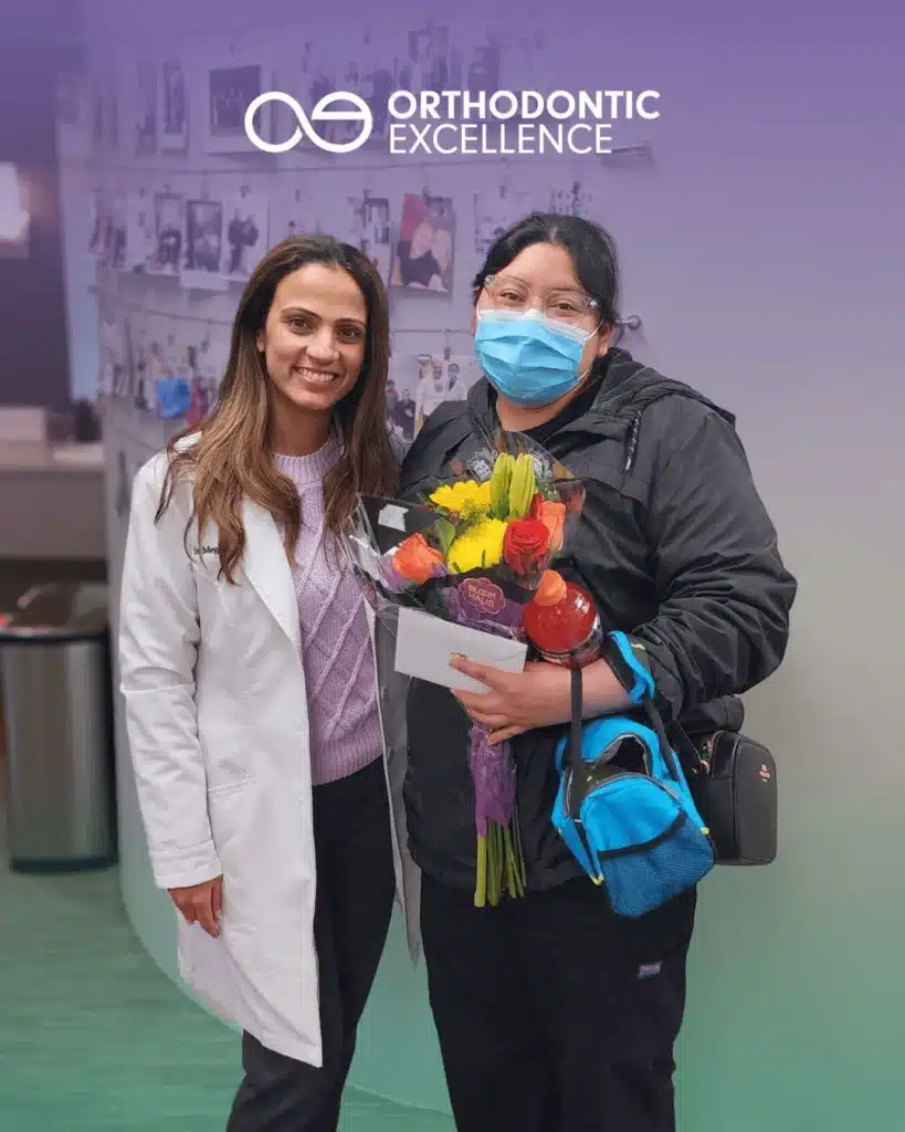 Dr. Megha Anand and a patient at Orthodontic Excellence, who is holding a bouquet of flowers.