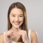A smiling woman holding a clear plastic aligner tray.