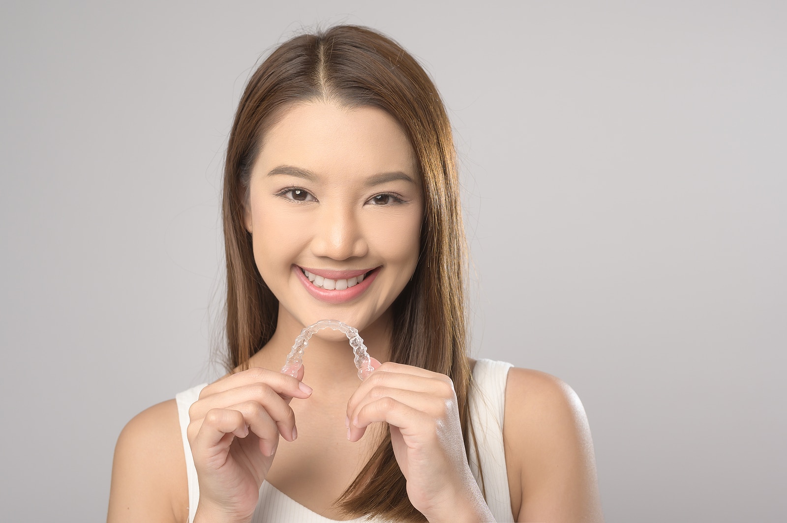 A smiling woman holding a clear plastic aligner tray.